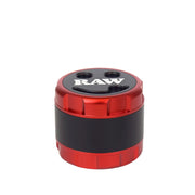 RAW brand modular steel pusher mill grinder shown with its red and black cylindrical container, open lid, inner chamber, and two silver metal milling plates